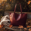 Bordeauxrote Ledertasche auf einer Holzbank mit Herbstlaub
