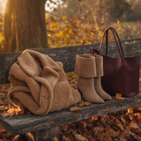Teddy-Mantel, Wildleder-Stiefel und Ledertasche auf einer Holzbank
