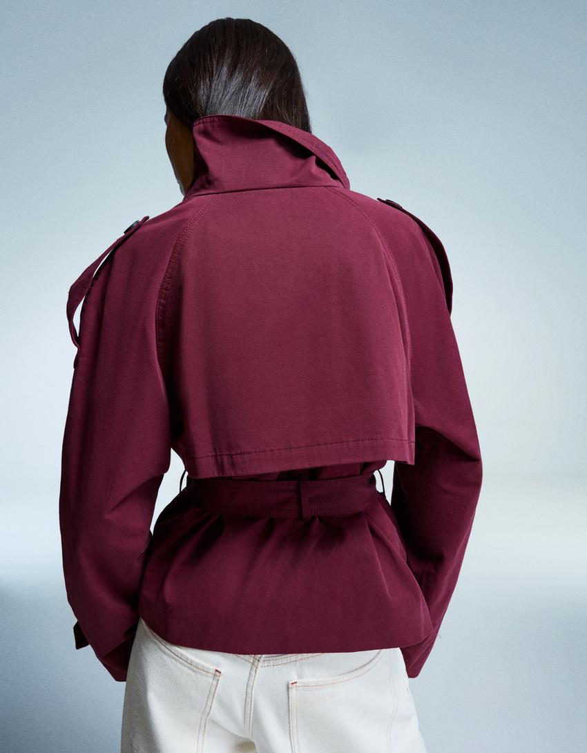 frau trägt bordeaux kurzen trenchcoat mit hohem kragen und gürtel