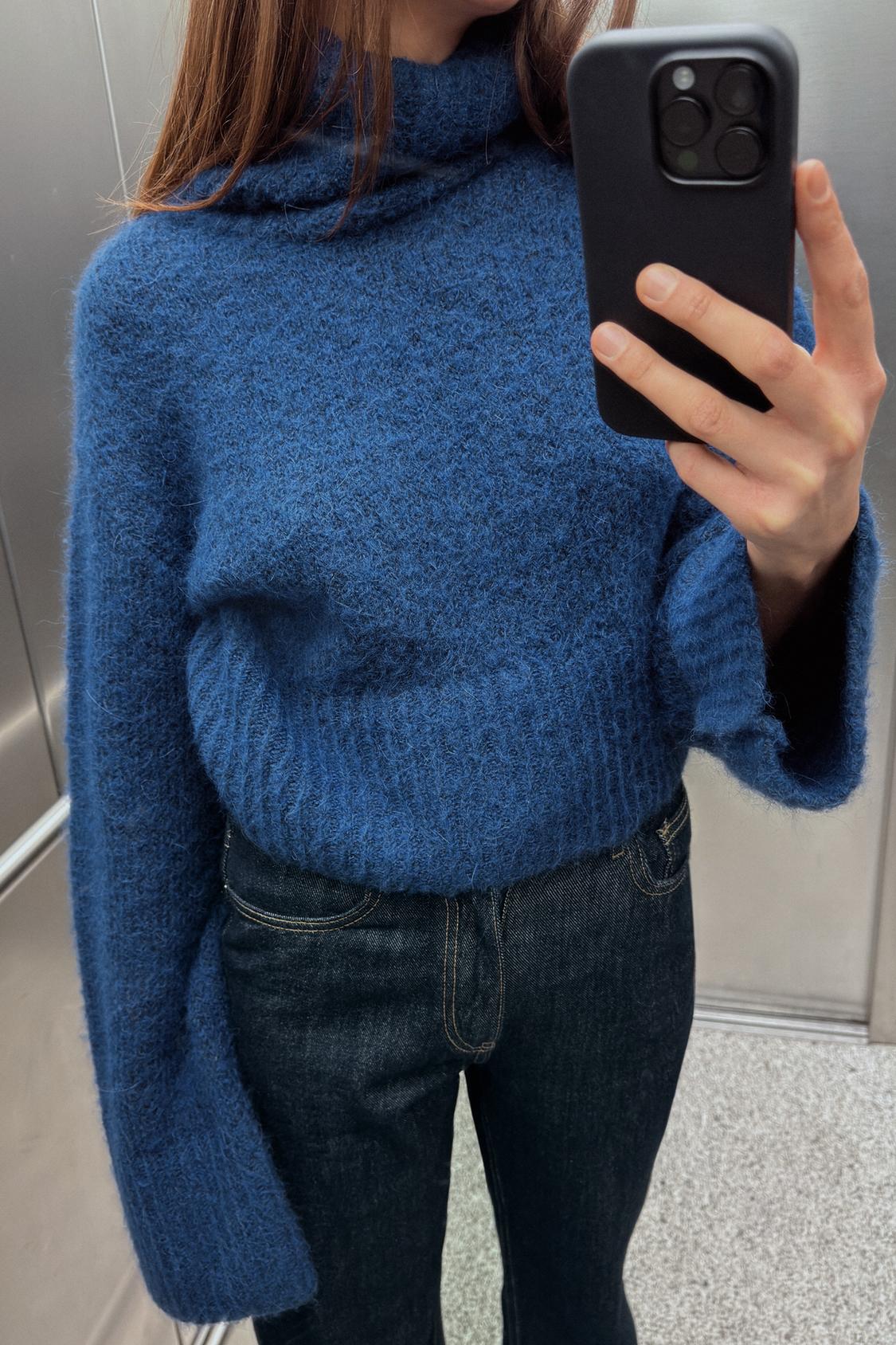 frau trägt blauen cropped strickpullover mit rollkragen und weiten ärmeln