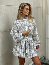 Vivianne Toile Dress in wit met grijze print, romantische mini jurk met ballonmouwen en strikceintuur, zomerse boho jurk, stijlvolle casual look.