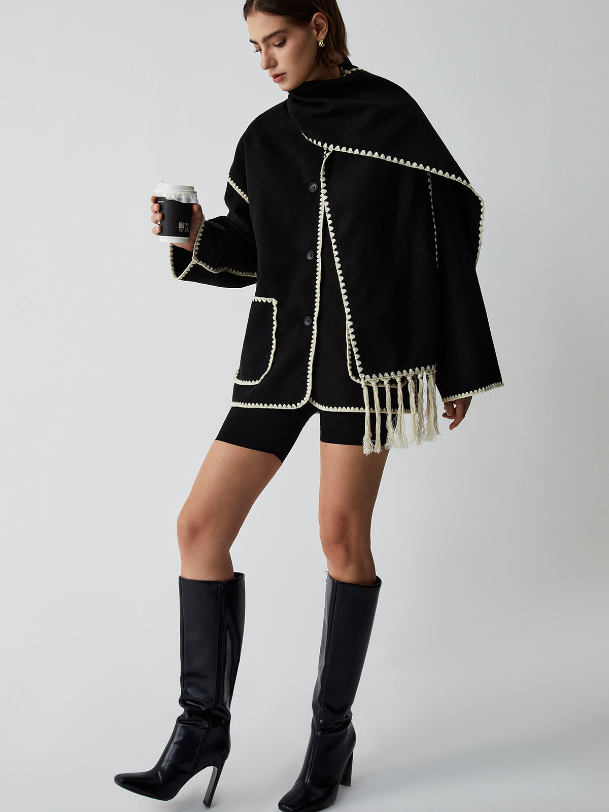 Model draagt zwarte cape met franjes
