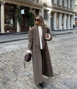 Model draagt Vesper Luxe Coat in bruin met casual outfit en zonnebril
