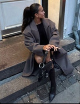 Vesper Luxe Coat in bruin gedragen op een bankje, casual gecombineerd
