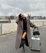 Model draagt de Vesper Luxe Coat beige met lichte jeans en oversized tas
