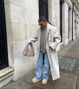 Model draagt de Vesper Luxe Coat beige met lichte jeans en oversized tas
