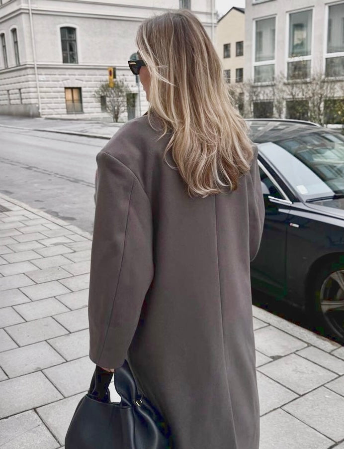 Achteraanzicht van de Vesper Luxe Coat bruin, gecombineerd met een lichte outfit
