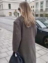 Achteraanzicht van de Vesper Luxe Coat bruin, gecombineerd met een lichte outfit
