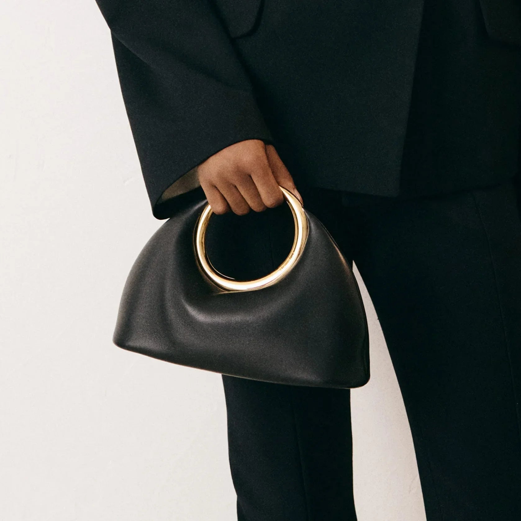 ivorene ringhandtasche mit goldenem henkel gestylt zu schwarzer hose und sandalen