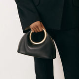 ivorene ringhandtasche mit goldenem henkel gestylt zu schwarzer hose und sandalen