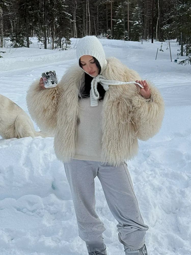 frau trägt beigen kunstpelzmantel im schnee mit weißen hosen