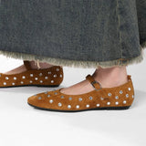 vrouw draagt bruine suède flats met rivets onder een denim rok
