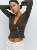 Model trägt braunen Cardigan mit weißen Jeans und goldenen Ohrringen