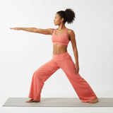 Modell in Aveline Wide-Leg-Hose Koralle und Sport-BH, Yoga-Krieger-Pose mit fließendem Stretch-Stoff