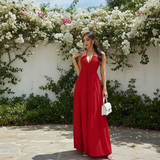 Modell trägt Liora Halter-Maxikleid in Rot mit weißer Handtasche, vor Bougainvillea-Blüten