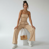 Elvani Lounge-Set Damen in Beige – sitzende Pose mit Bandeau-Top, Wide-Leg-Hose und Korb-Handtasche